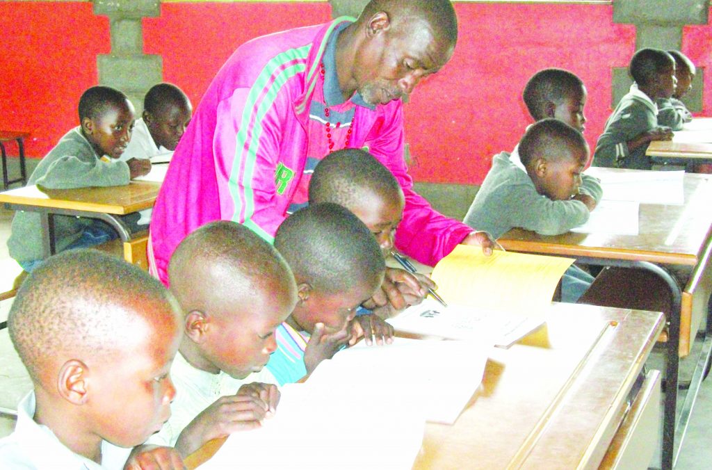 The only teacher at Ntamaha Primary School, Mr Matsa Monaheng assists one of the class one pupils while the other classes concentrate on their own work